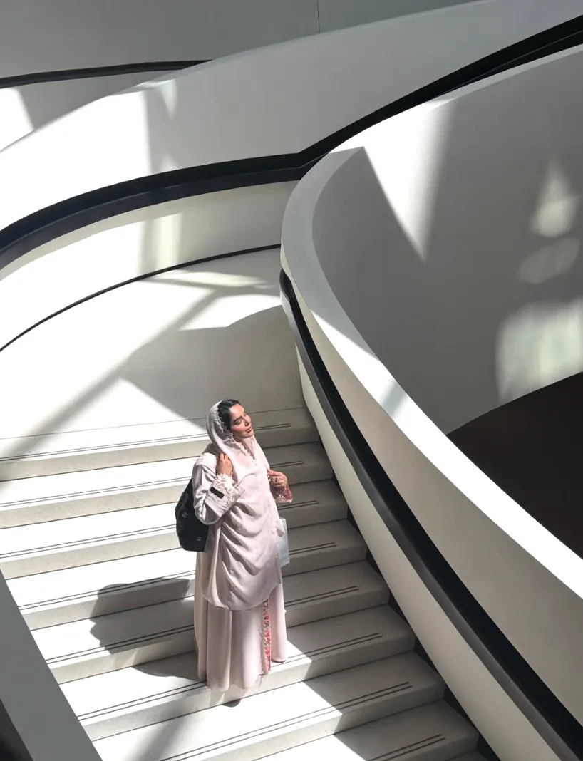 Emirati creator in a pastel abaya and sheila on a sculpted white staircase